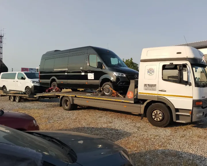 Crni kombi na transportnoj platformi belog kamiona.