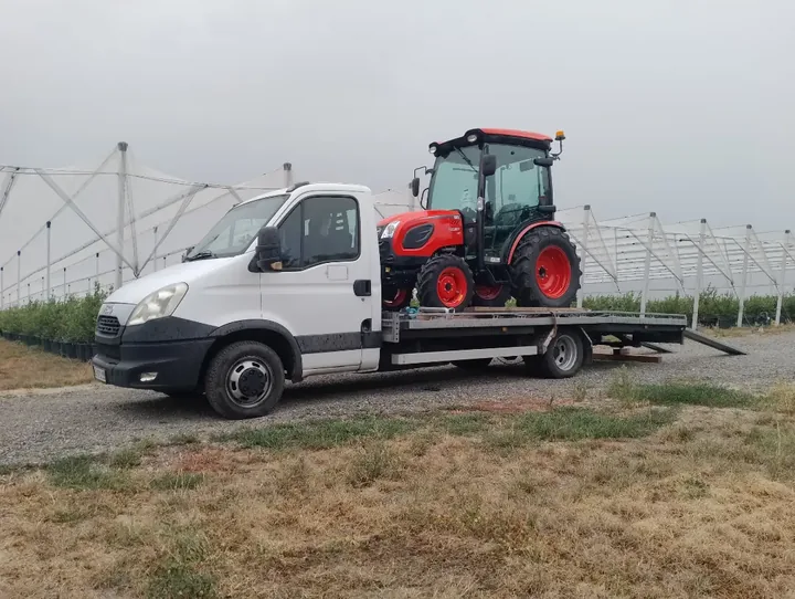 Kompaktni crveni traktor na platformi dostavnog vozila.