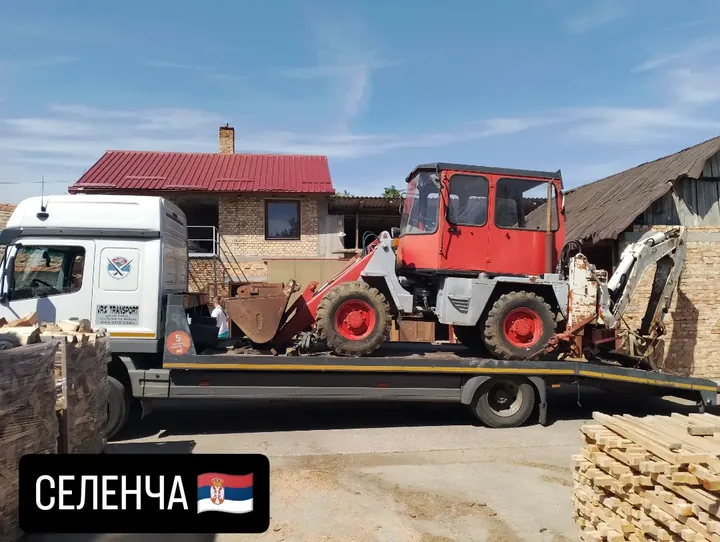 Crveni utovarivač sa kašikom na platformi kamiona.