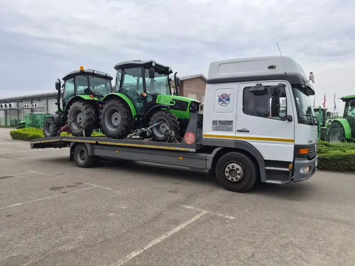 Zeleni traktor na platformi kamiona Mercedes-Benz Atego.
