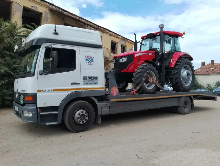 Crveni traktor na platformi belog kamiona.